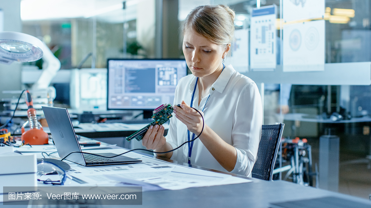 女計算機科學家將電路板連接到她的筆記本電腦并開始編程。她在先進技術實驗室工作。